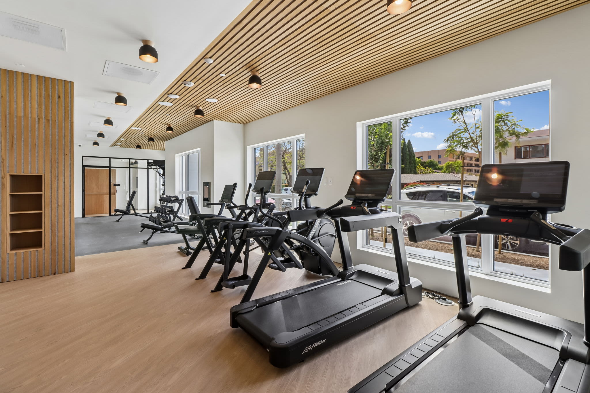 Fitness center with treadmills, cardio equipment, mounted screens, and wood‑look flooring at Treehouse in San Diego, California.