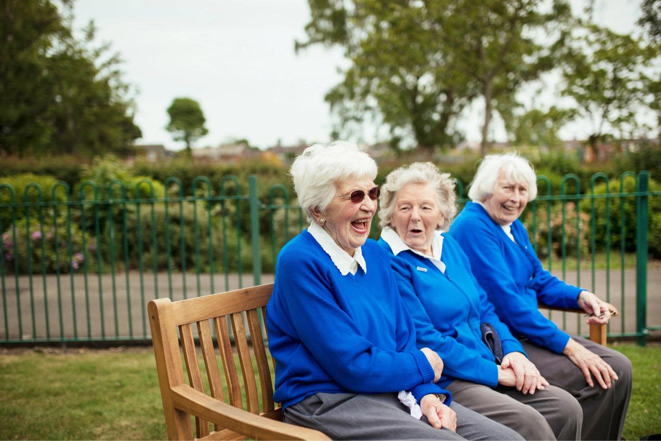 Three senior citizens sitting on a bench together and laughing