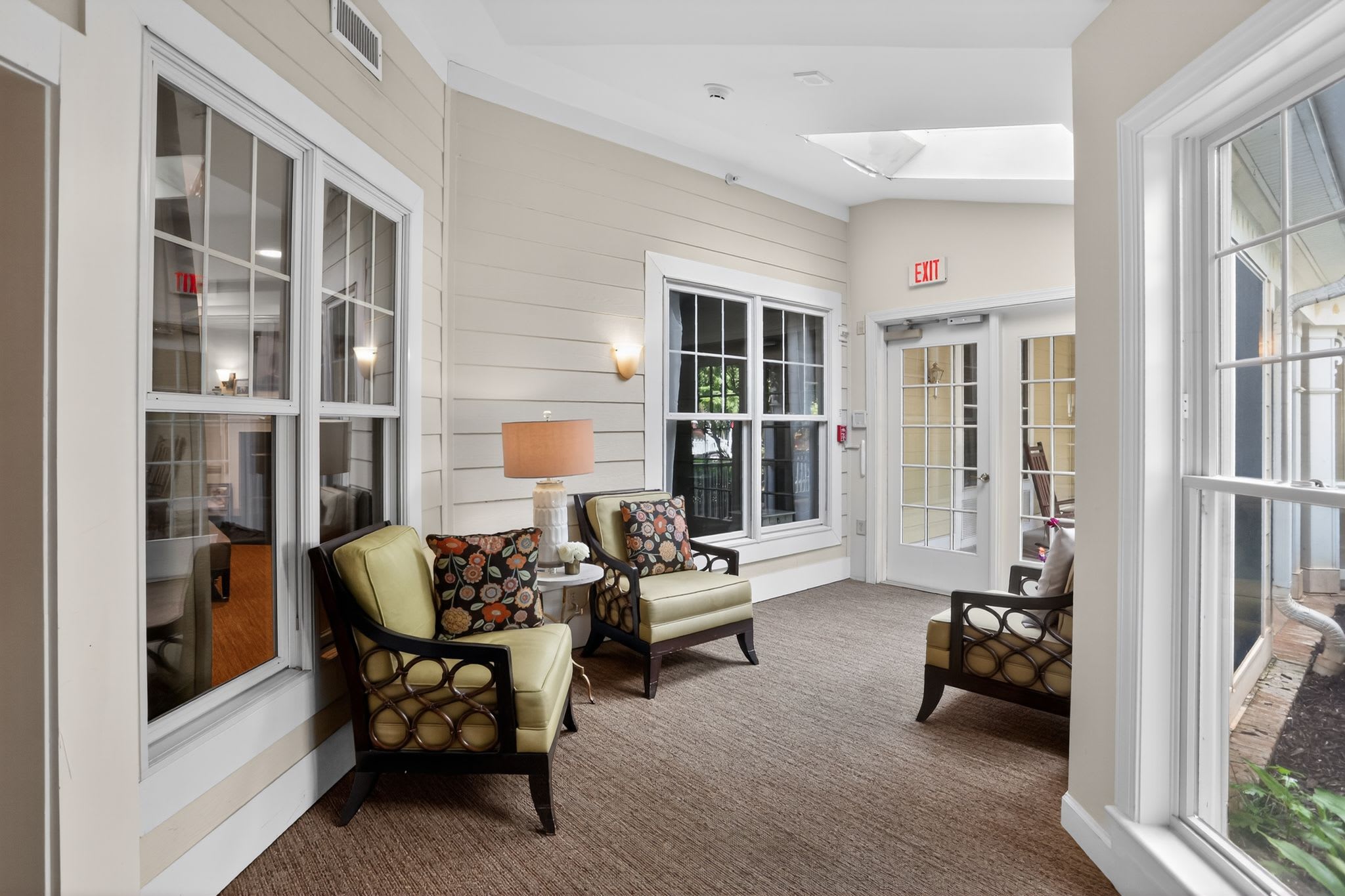 Sitting area with chairs and large windows overlooking an outdoor patio at Glenncrest at Johns Creek in Johns Creek, Georgia.