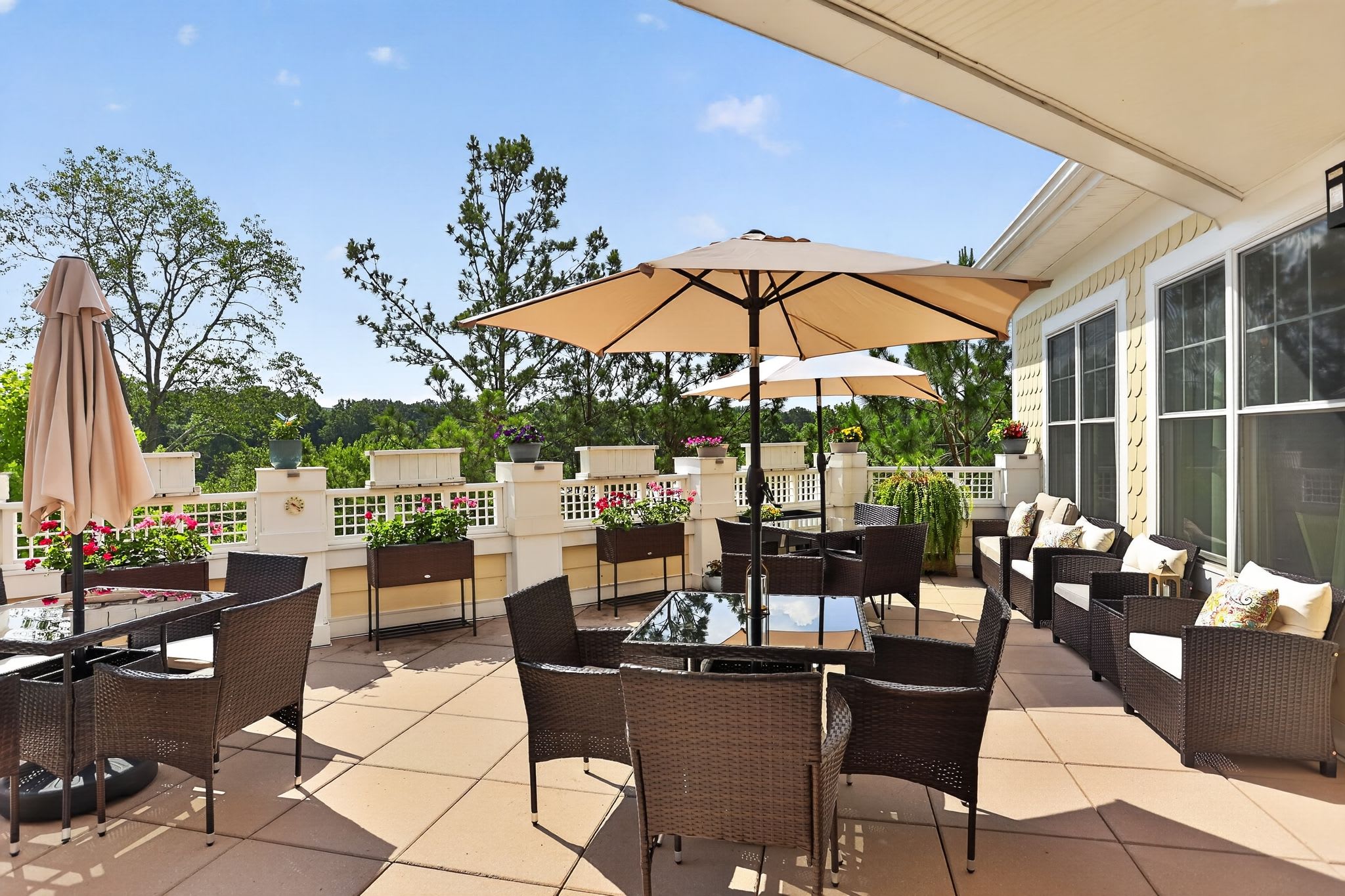 Outdoor patio with wicker seating, tables, umbrellas, and potted flowers overlooking a landscaped area at Glenncrest at Johns Creek in Johns Creek, Georgia.