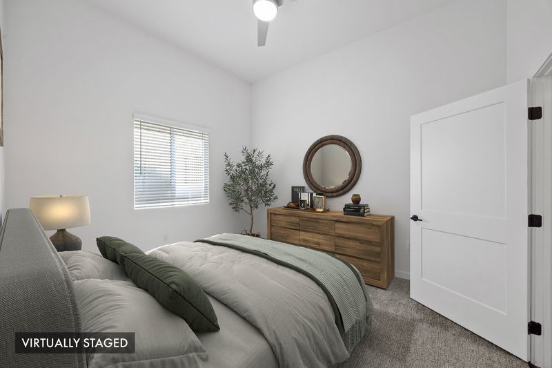 Primary bedroom with plush carpeting, wood dresser, large window, and contemporary furnishings at Canyon Bluffs Apartment Homes in Riverside, California