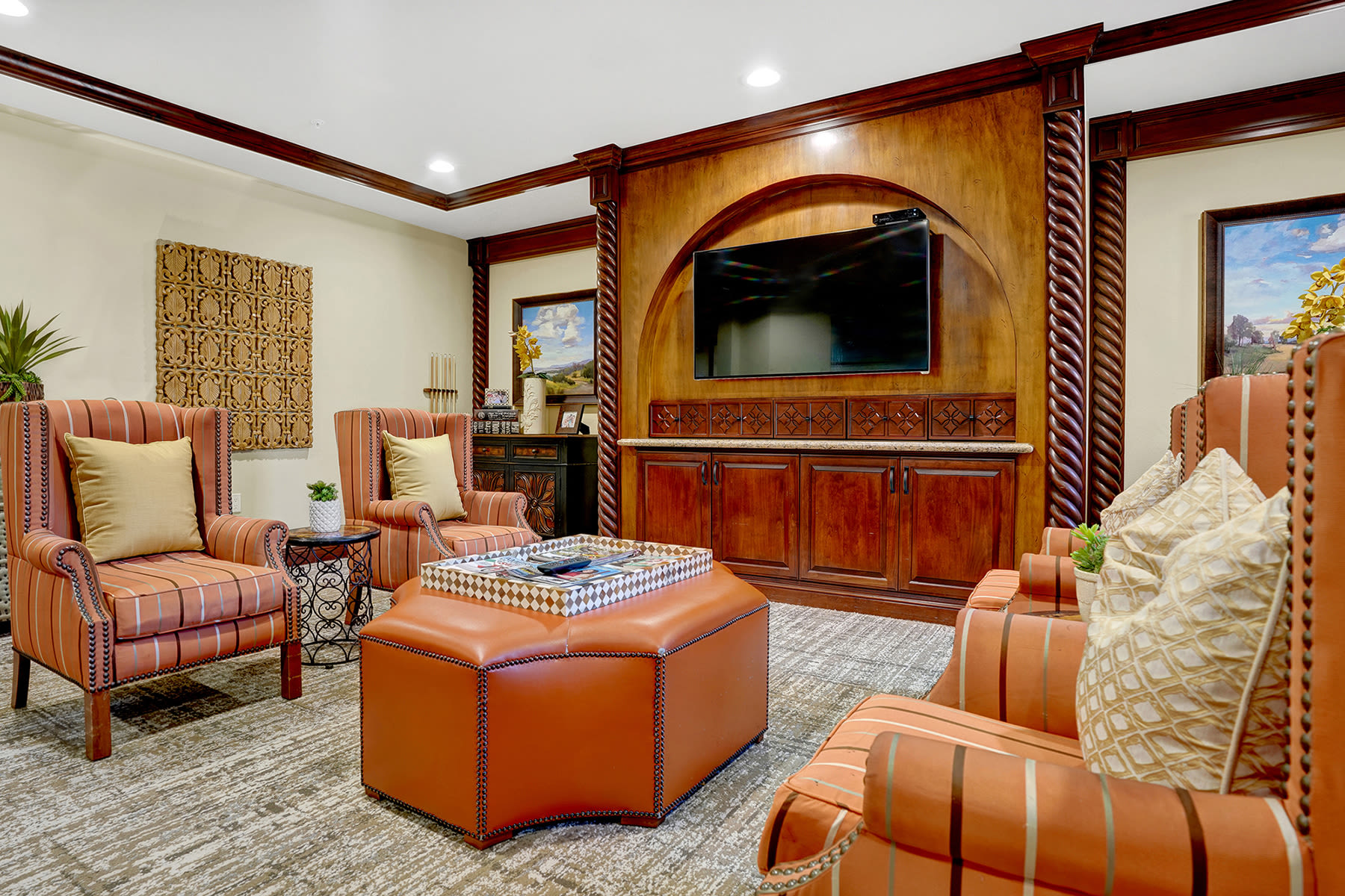 Cozy senior living lounge with upholstered chairs and TV entertainment wall at Estancia Del Sol in Corona, California