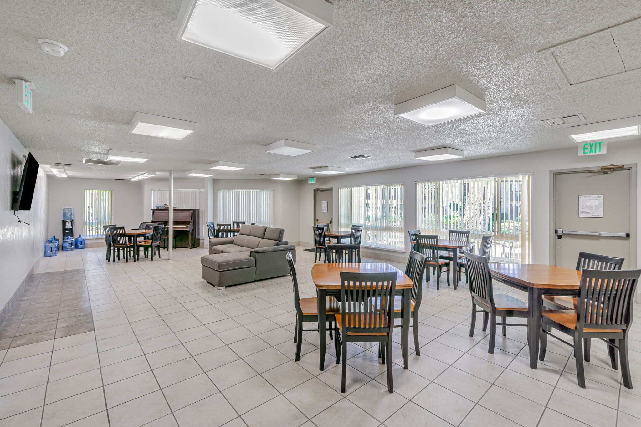 Bright community room with tables, chairs, lounge seating, and large windows at Clayton Gardens in Concord, California