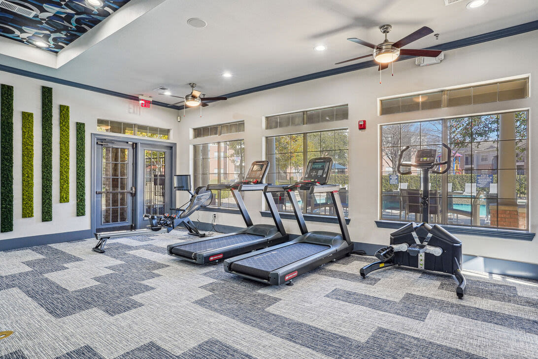 Fully-equipped gym with treadmills, flat-screen TVs, and ceiling fans at Mission Eagle Pointe in Allen, Texas, 