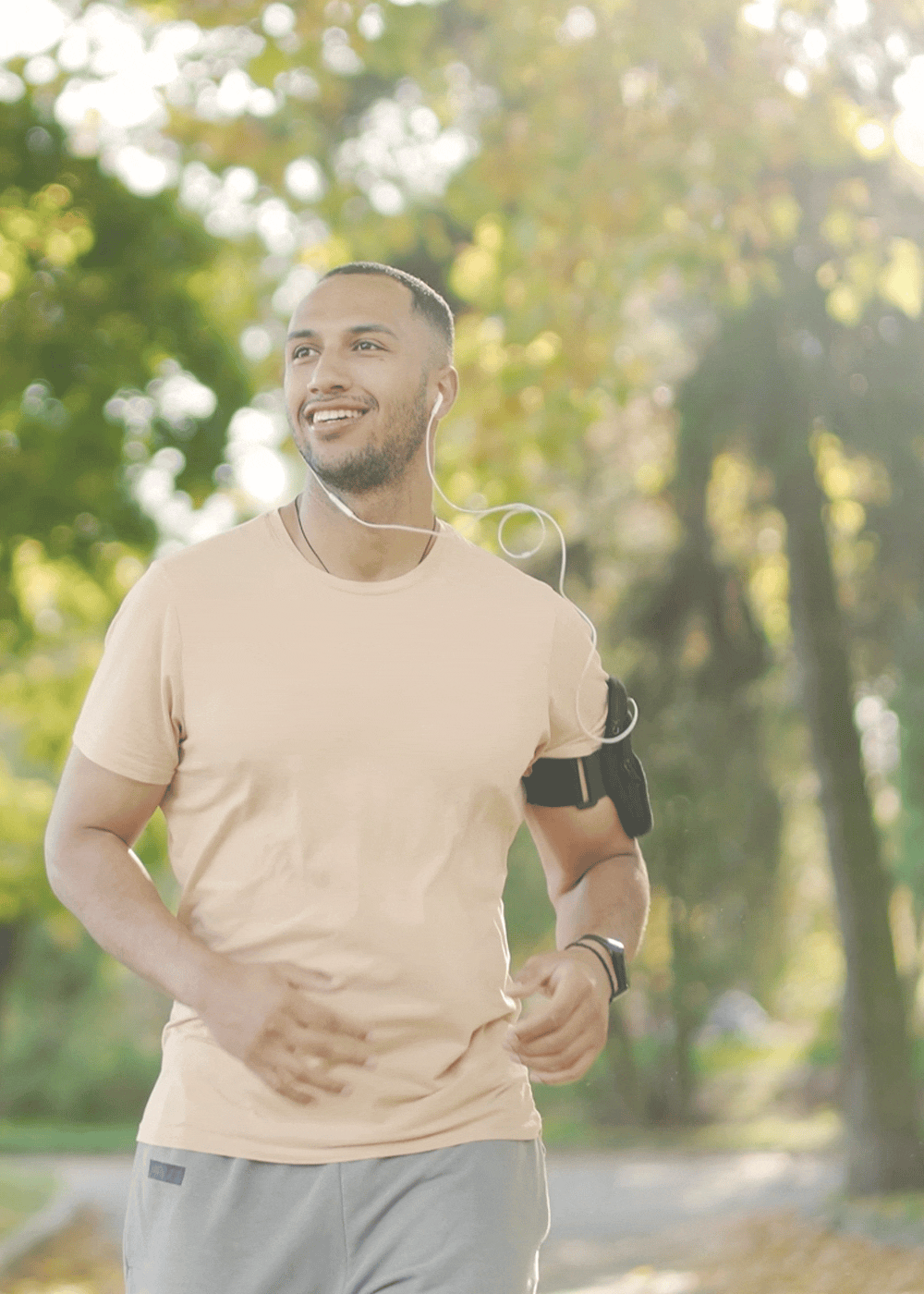 Resident jogging outdoors on a sunlit path surrounded by green trees wearing earphones at The Indie Glendale Collection in Glendale, California