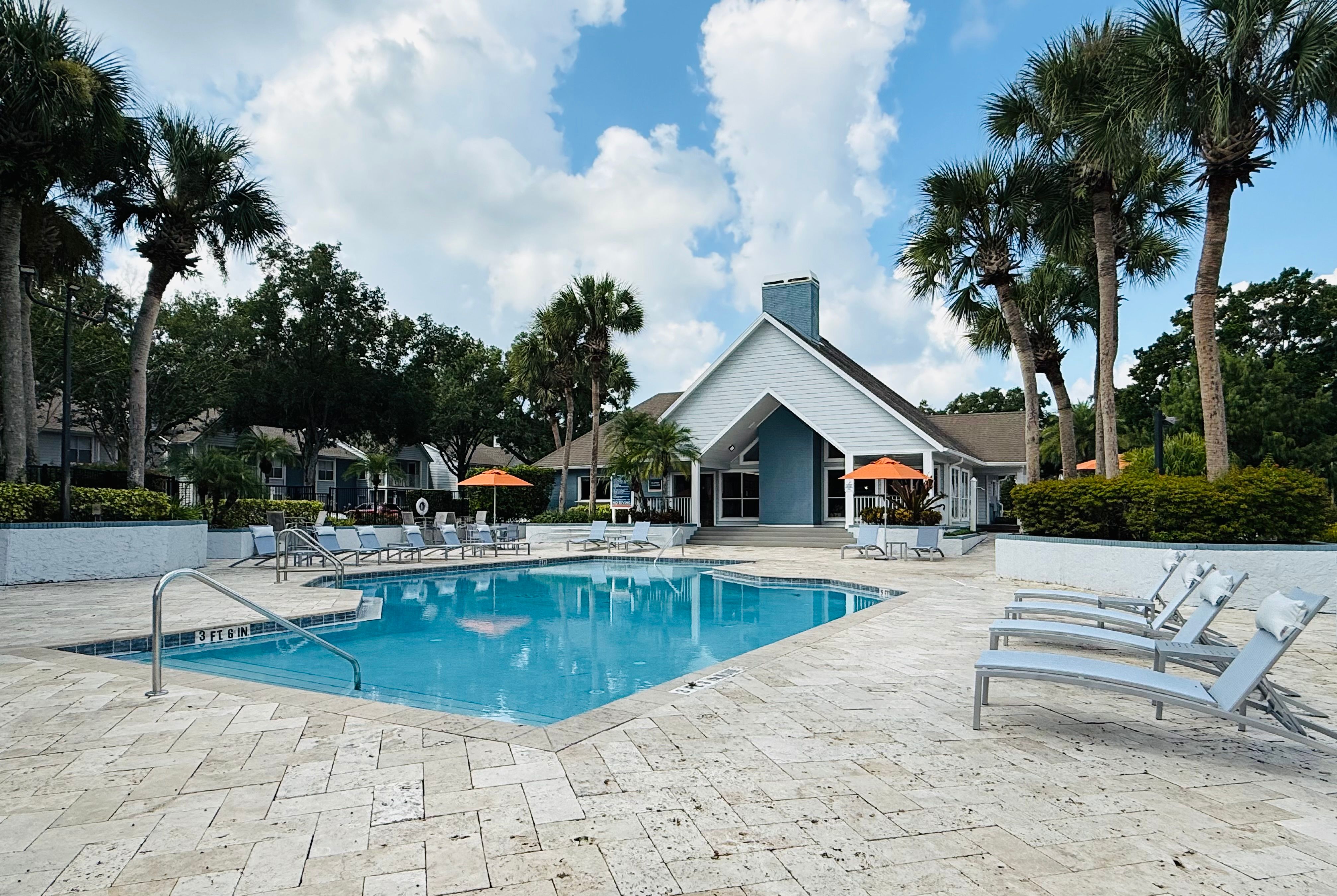 Outdoor pool with lounge chairs and a clubhouse surrounded by palm trees at Tuskawilla at Winter Springs in Winter Springs, Florida