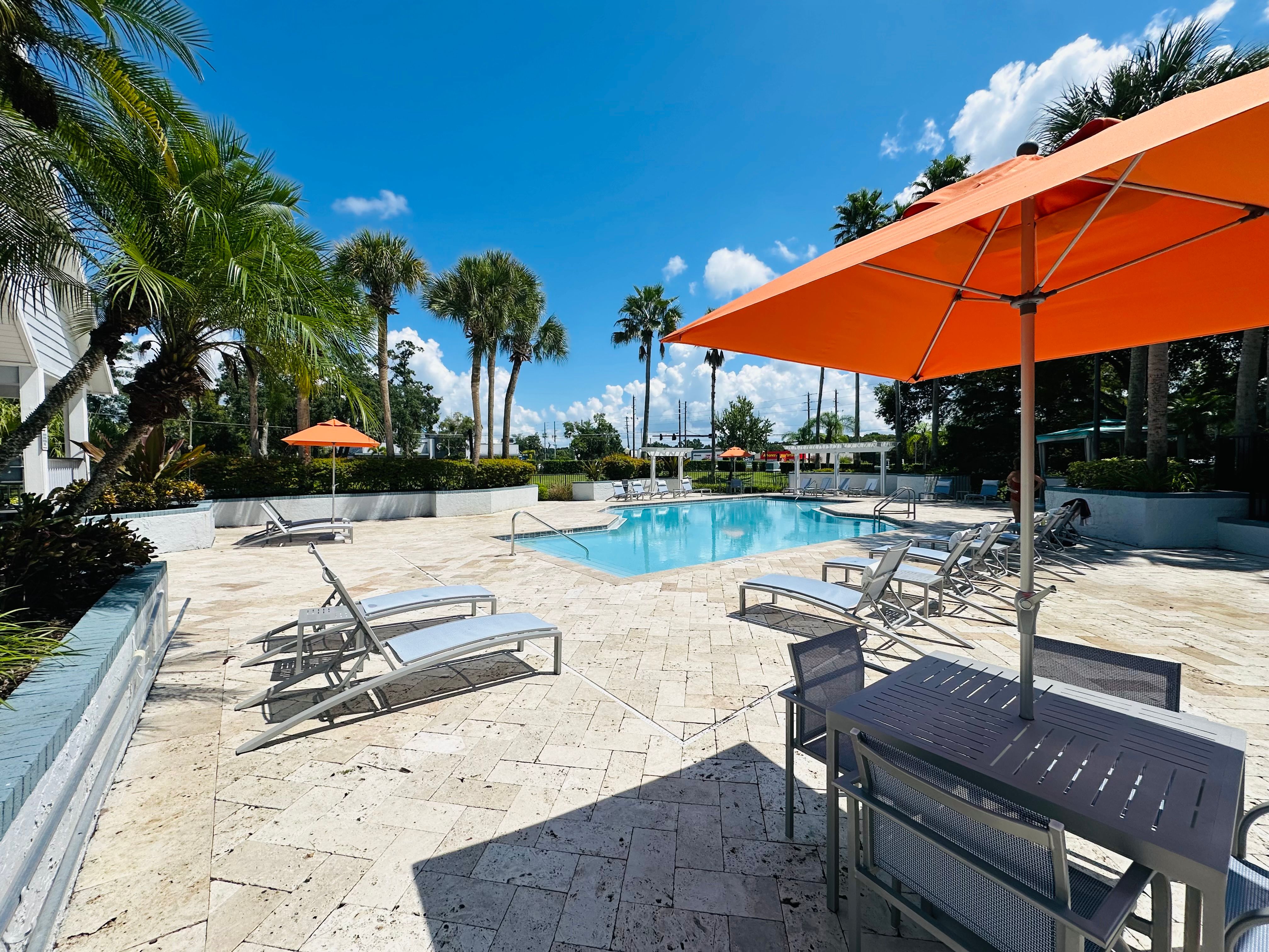 Sunny pool deck with lounge chairs and orange umbrellas beside a clear outdoor pool at Tuskawilla at Winter Springs in Winter Springs, Florida