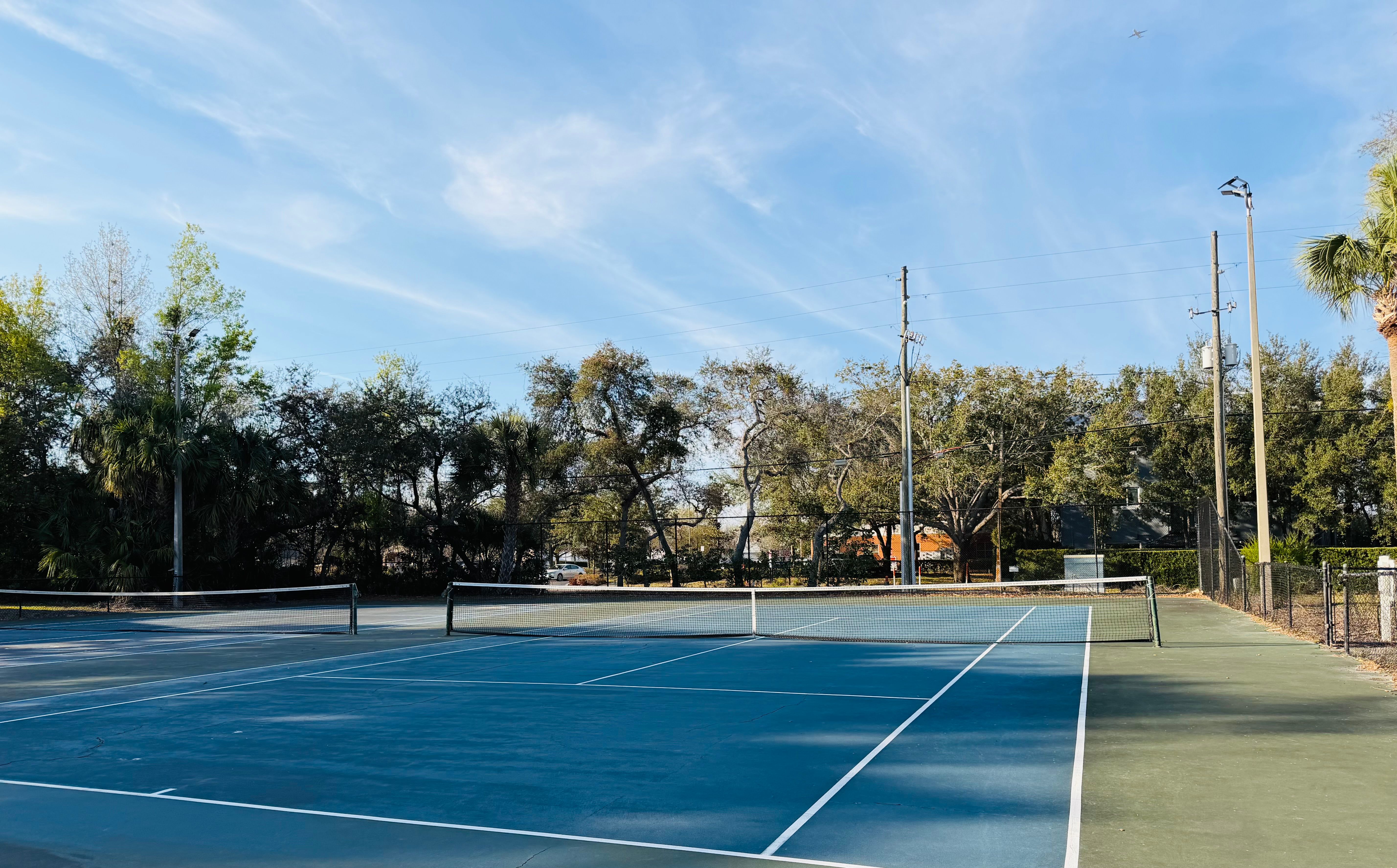 Outdoor tennis court with blue playing surface surrounded by trees under a clear sky at Tuskawilla at Winter Springs in Winter Springs, Florida