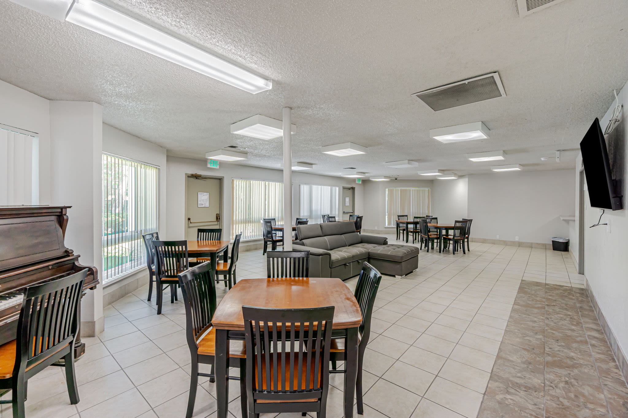Spacious community room with tables, chairs, a piano, and lounge seating in a bright area at Clayton Gardens in Concord, California