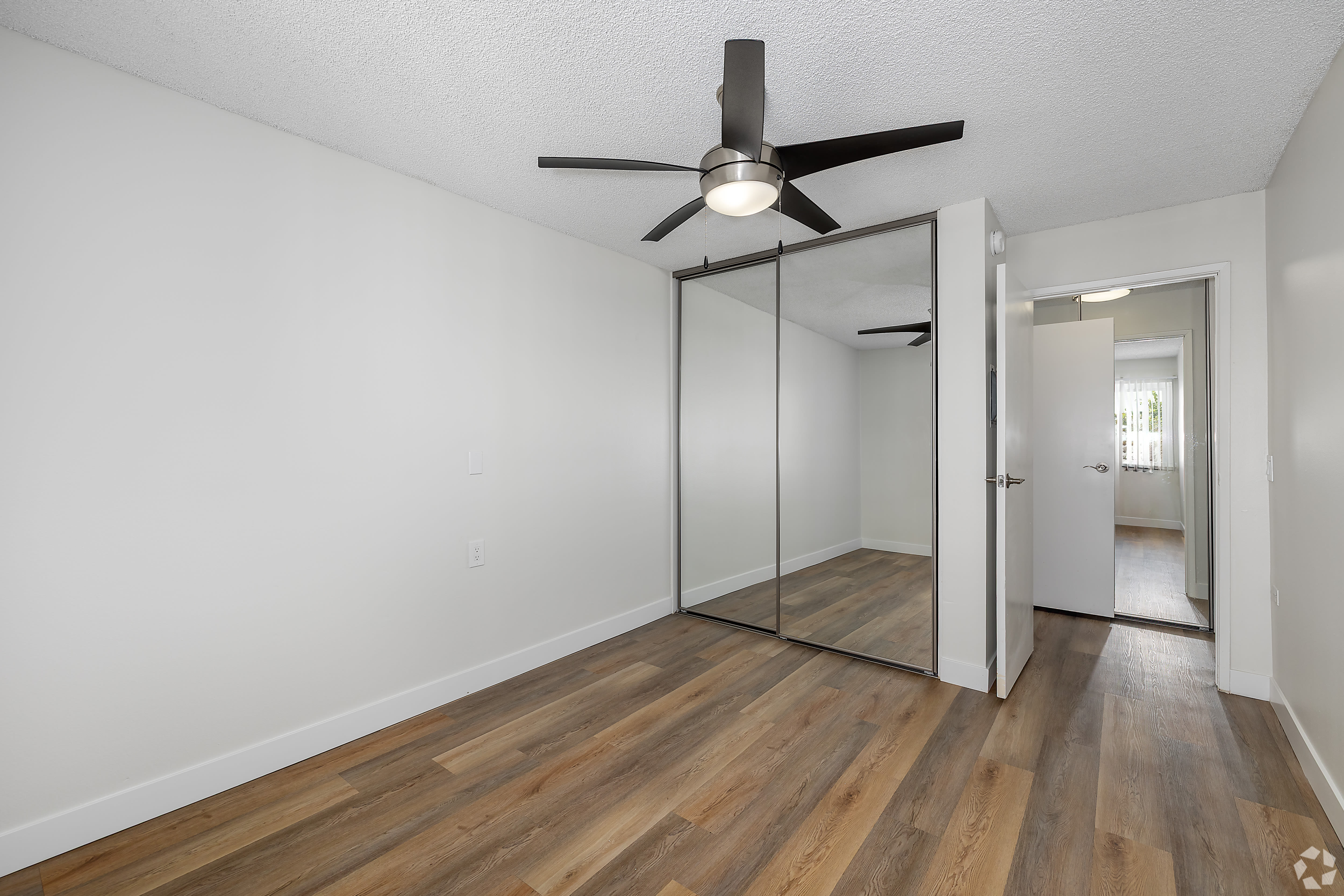 Bedroom with mirrored closet doors, ceiling fan, and wood flooring at Beck Park in North Hollywood, California