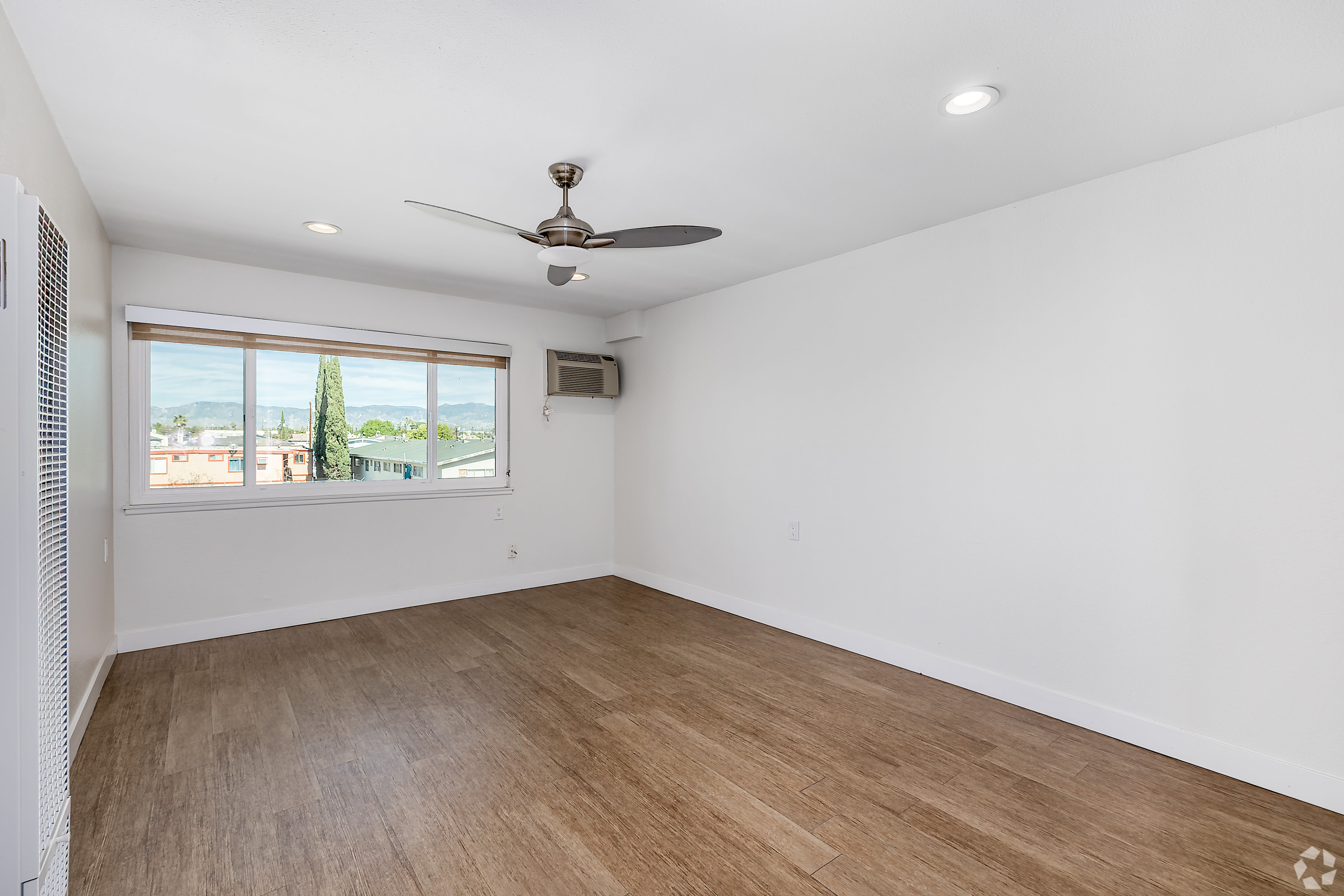 Spacious room with wide window, ceiling fan, and wood flooring at Beck Park in North Hollywood, California