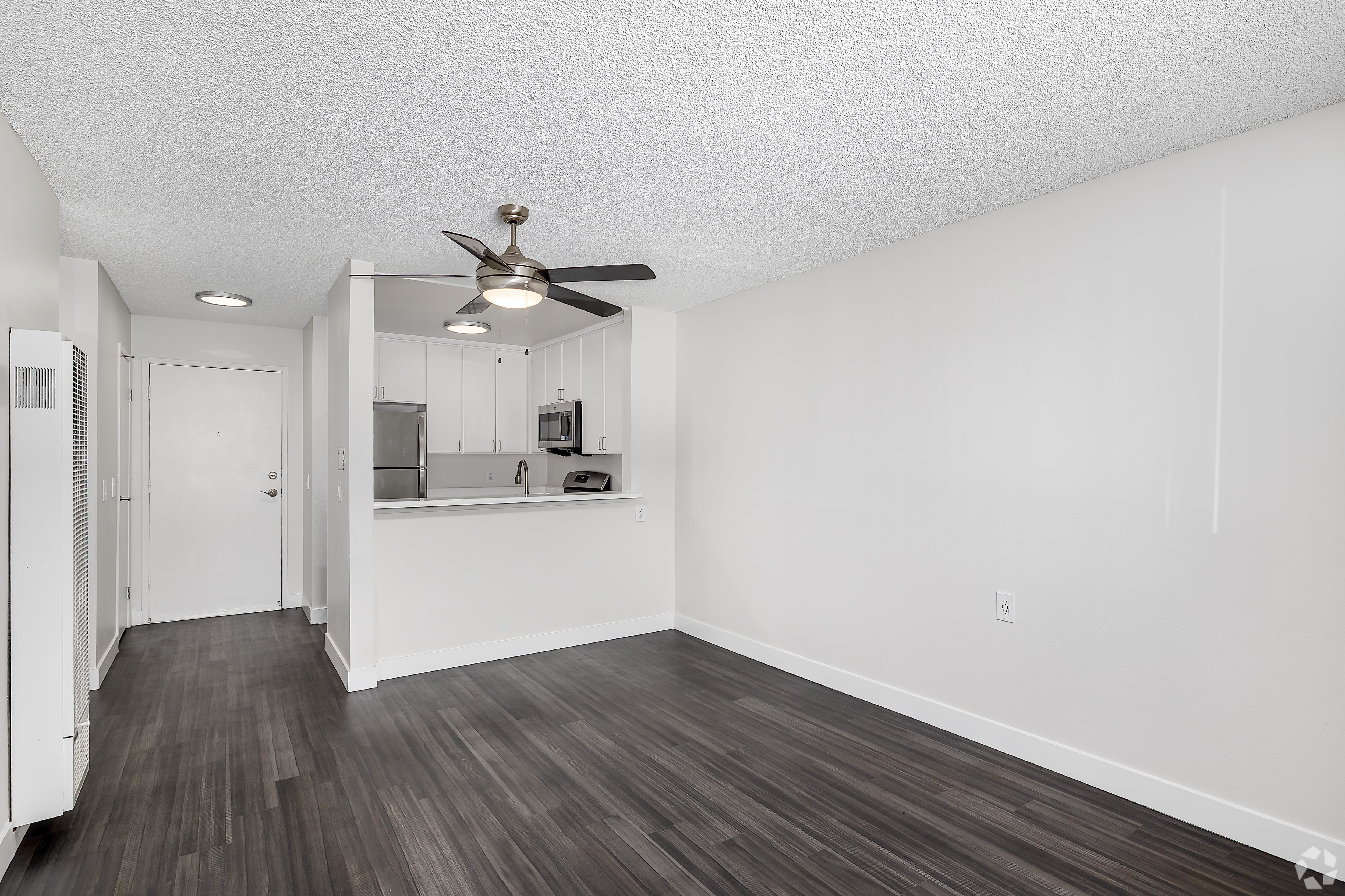 Living area with dark wood floors, ceiling fan, and open kitchen at Beck Park in North Hollywood, California