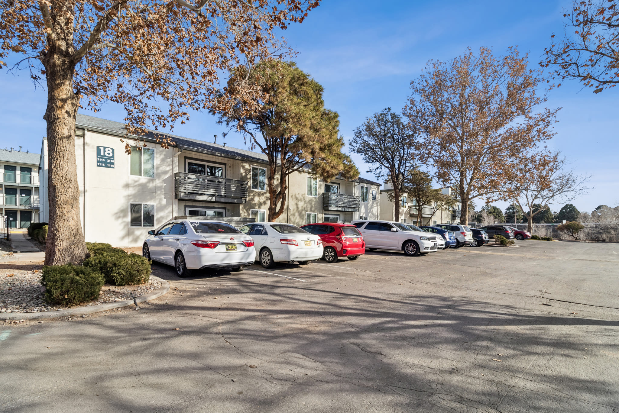 Apartment building with parked cars and trees on a sunny day at Pinewood Estates in Albuquerque, New Mexico