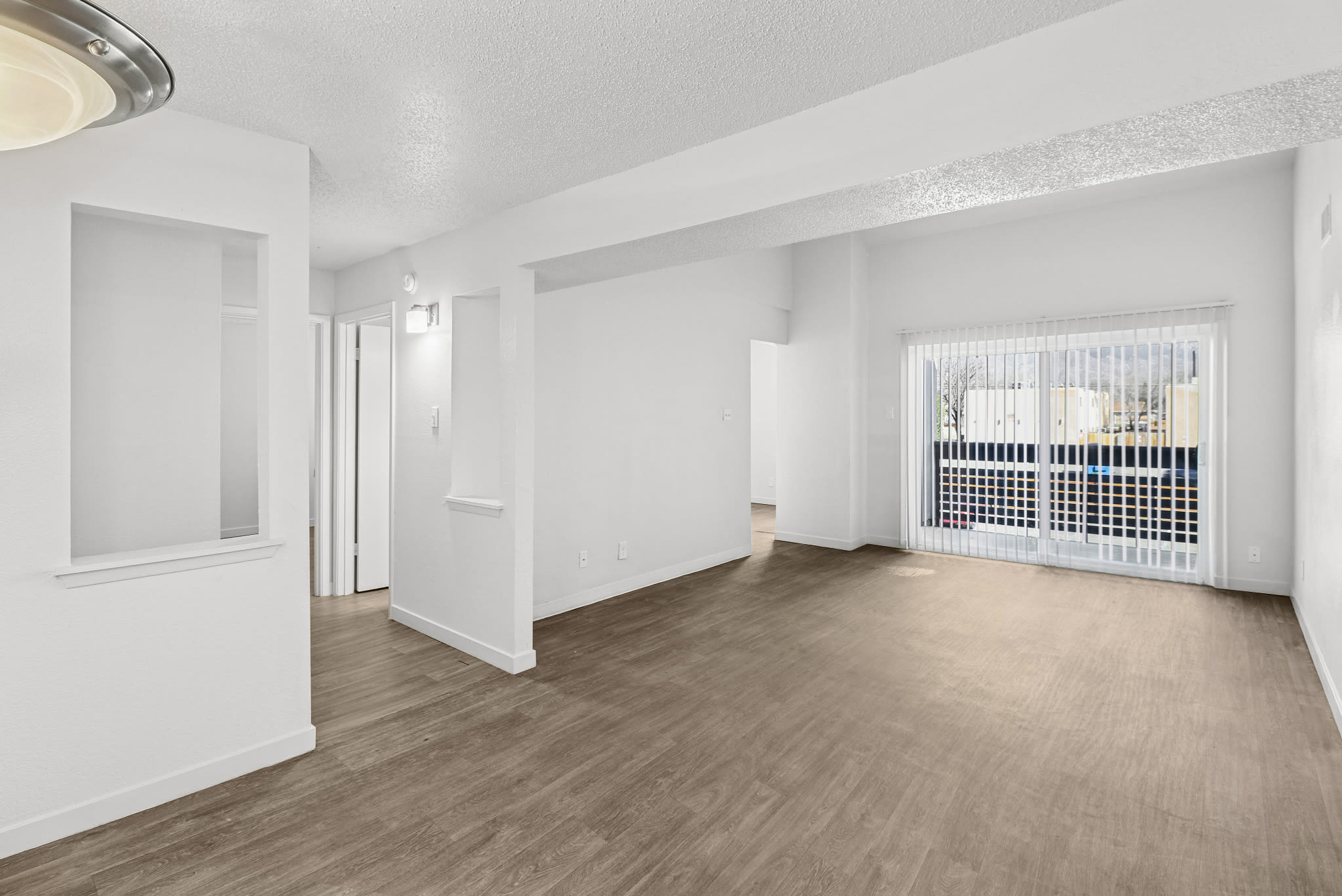 Open living area with wood‑style floors, white walls, and sliding glass door to a balcony at Pinewood Estates in Albuquerque, New Mexico  