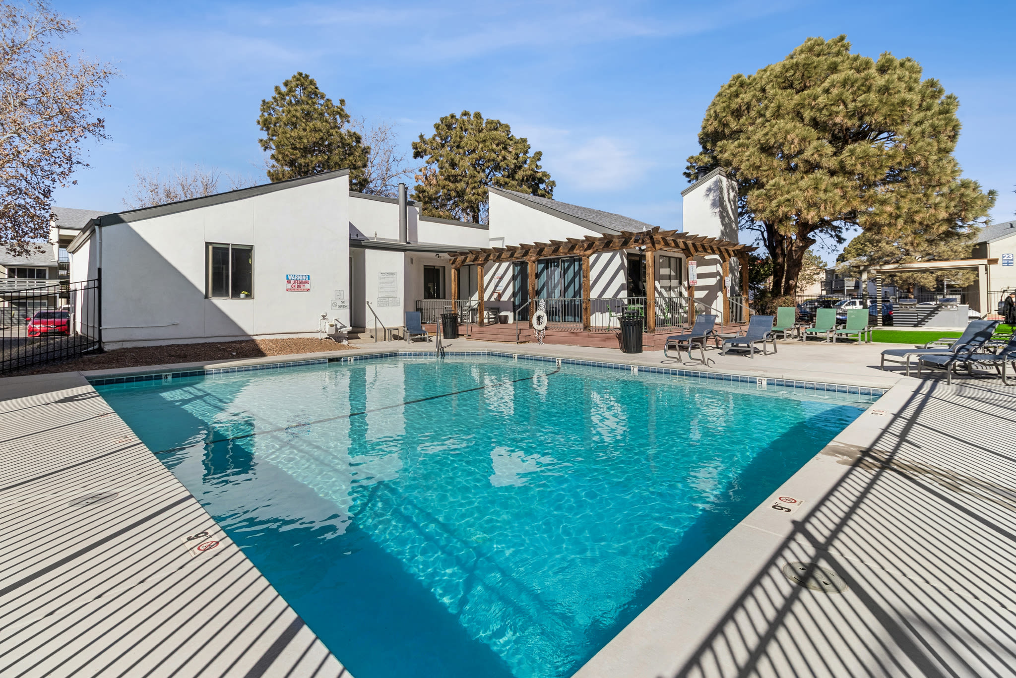 Outdoor pool with lounge chairs, pergola, and clubhouse surrounded by trees at Pinewood Estates in Albuquerque, New Mexico