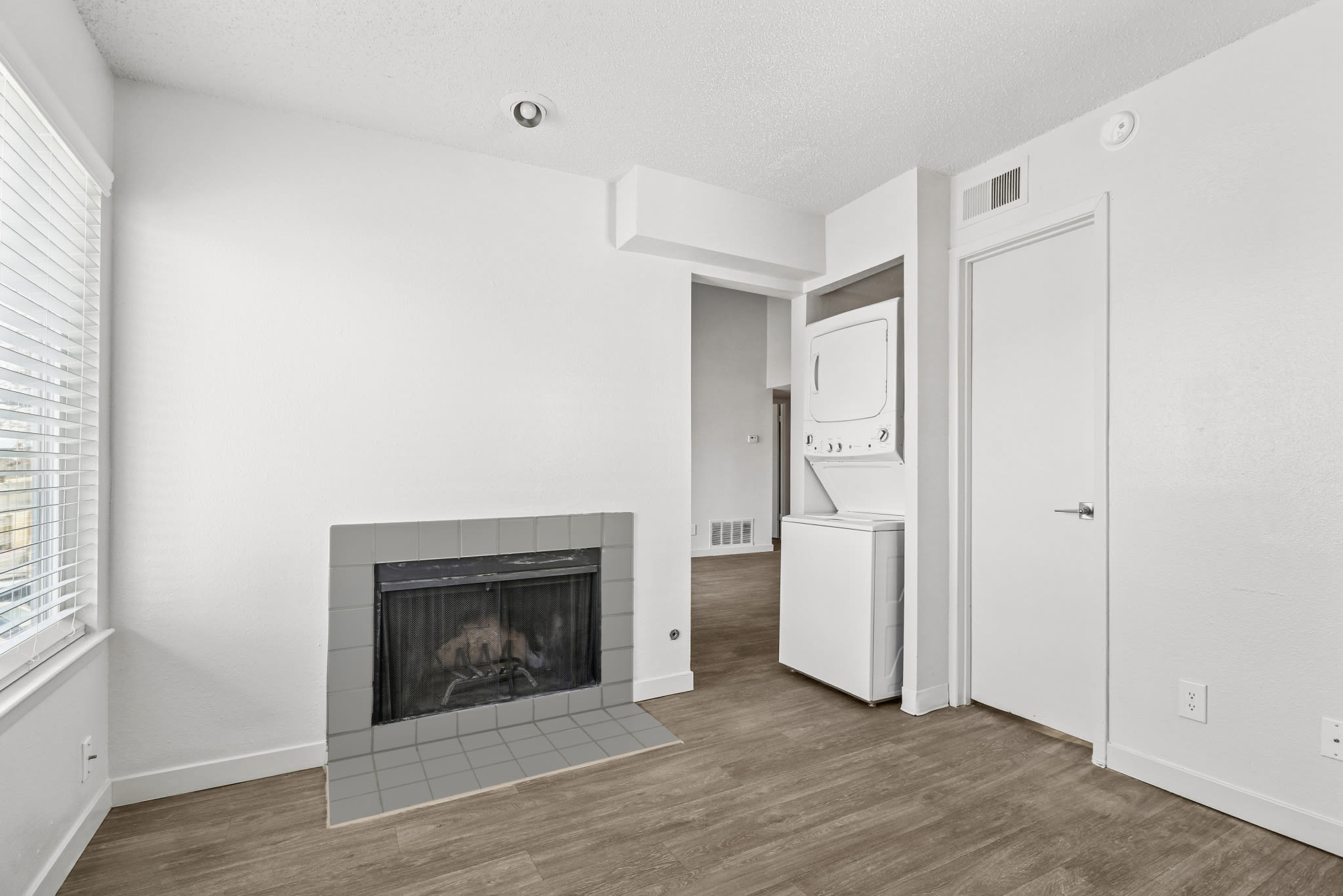 Living area with fireplace, wood‑style flooring, and stacked washer‑dryer unit at Pinewood Estates in Albuquerque, New Mexico