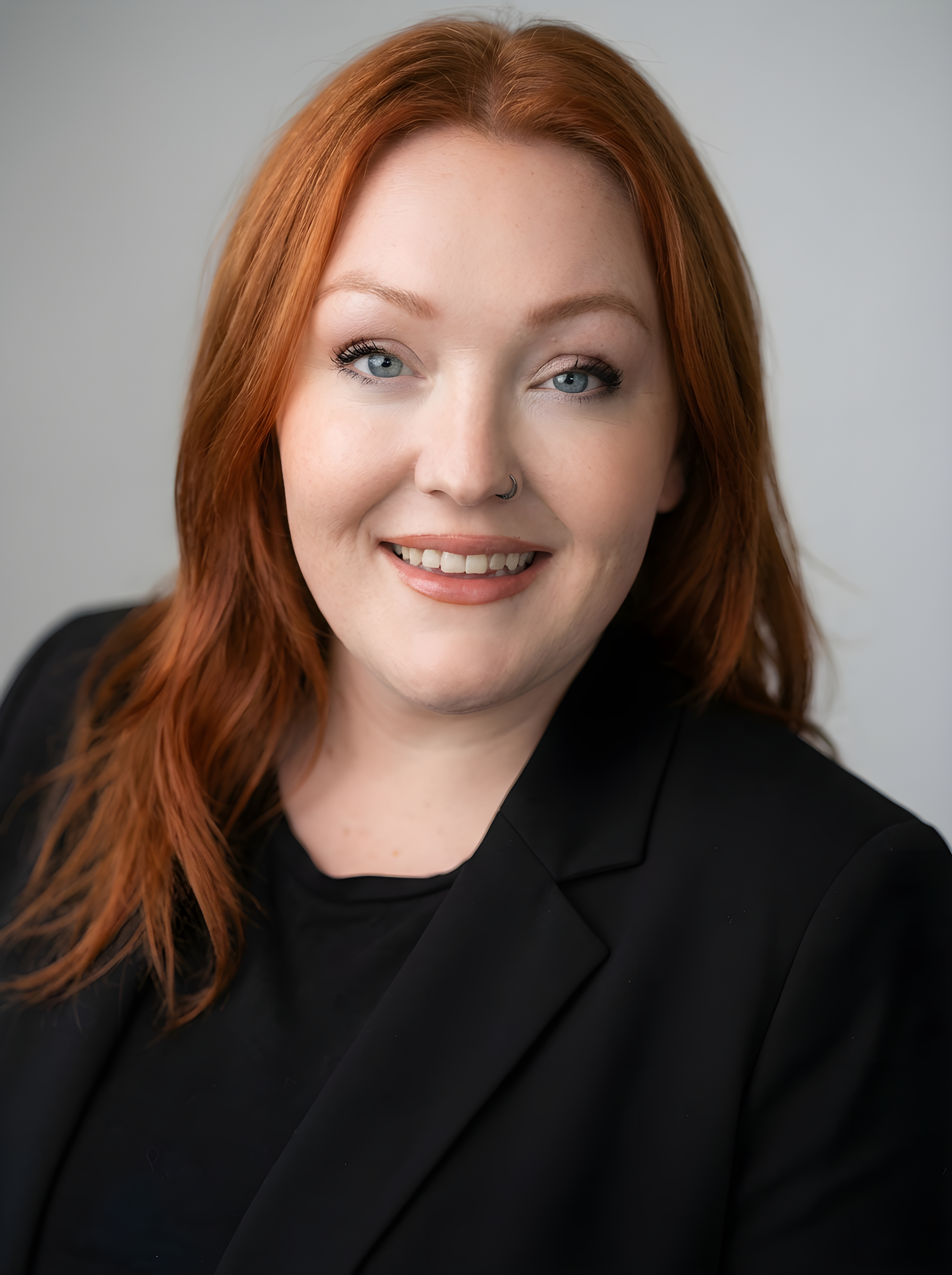Professional team member headshot with red hair and black blazer, studio portrait at ATX Fenton in Austin, Texas