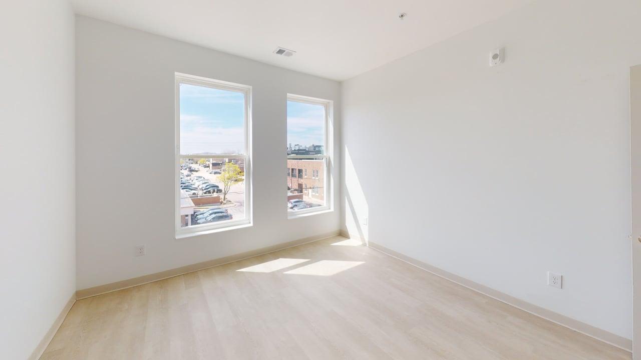 Bright bedroom with light wood floors, white walls, and two large windows for natural light at Terra Station in Hudsonville, Michigan