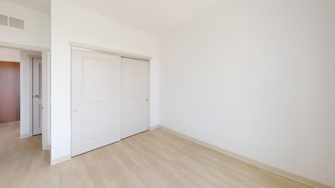 Empty bedroom with light wood flooring, white walls, and sliding-door closet at Terra Station in Hudsonville, Michigan