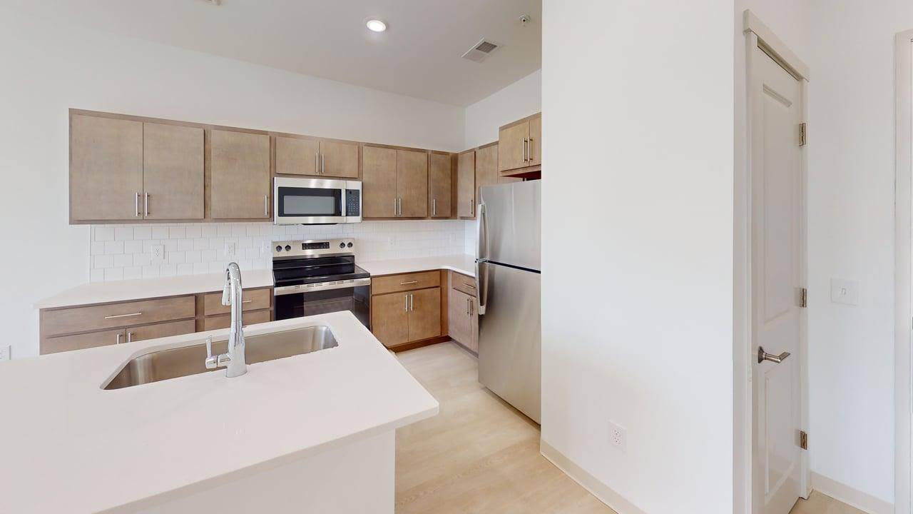 Modern kitchen featuring island sink, wood cabinetry, subway tile backsplash, and stainless appliances at Terra Station in Hudsonville, Michigan