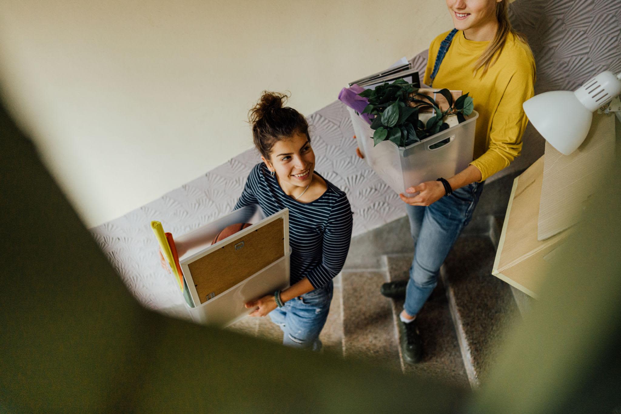 Students carrying storage bins and dorm belongings down a stairwell during college move-out day.