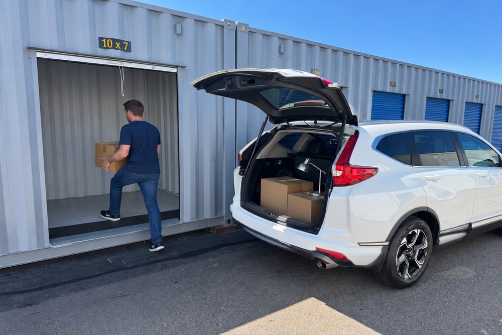 Man carrying a box from a white SUV into a clean 10 x 7 drive-up storage unit at CSI Mini Storage Alameda