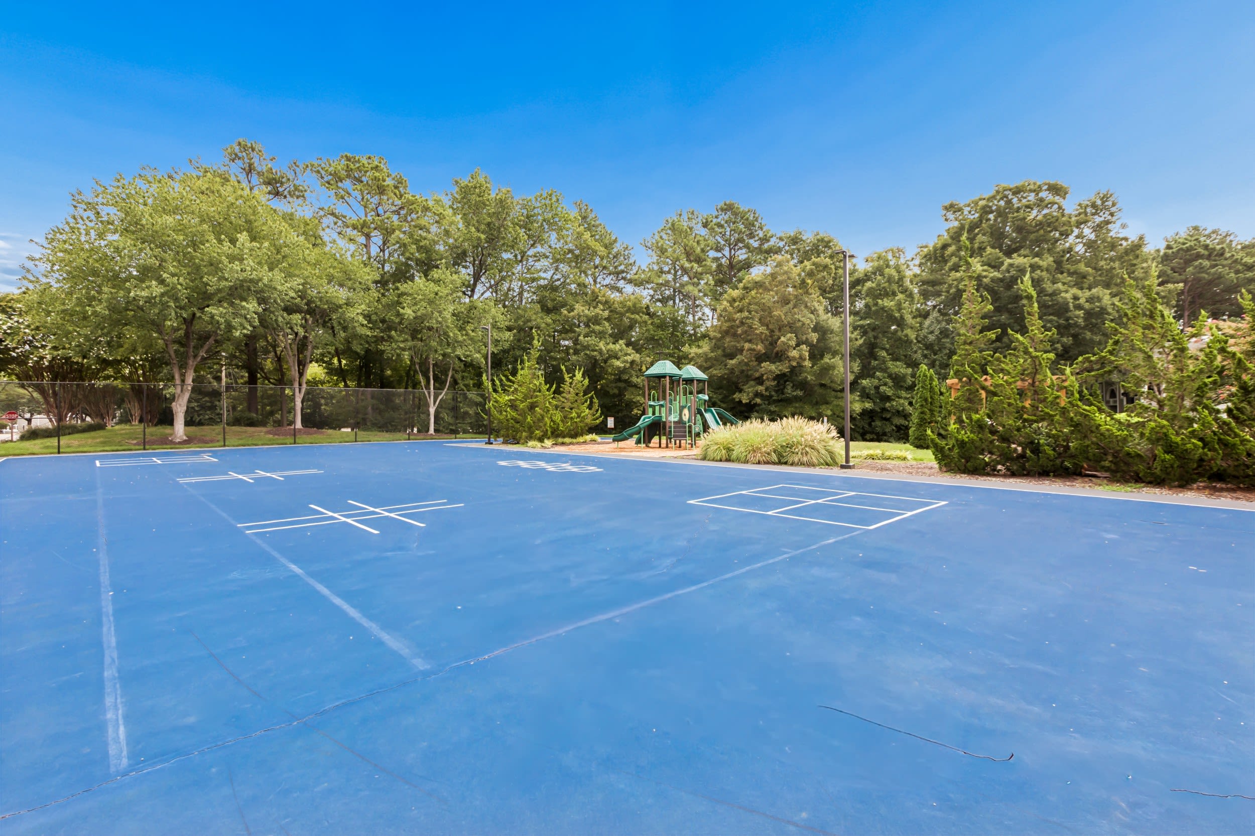 Pet-Friendly Apartments in Hioaks, VA - Reserve South - Outdoor Blue Multi-Sports Court With Chain-Link Fencing, and Nearby Playground Set Among Mature Trees and Green Landscaping.