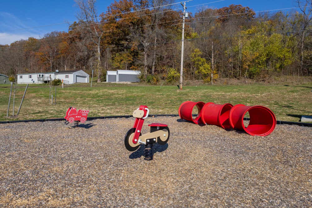 Playground with red toy fire truck, spring rider, and colorful tubes on a gravel surface at Kershaw Greene III in Athens, Ohio