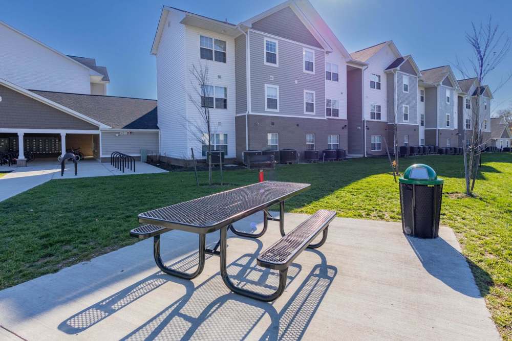 Outdoor picnic area with a table and trash can, green lawn and multi-story apartment buildings in background at Kershaw Greene III in Athens, Ohio