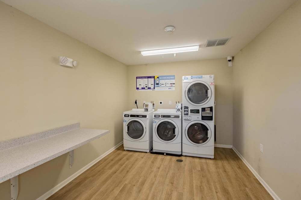 Laundry room with three washing machines, white countertops, and wood-style flooring at Kershaw Greene III in Athens, Ohio