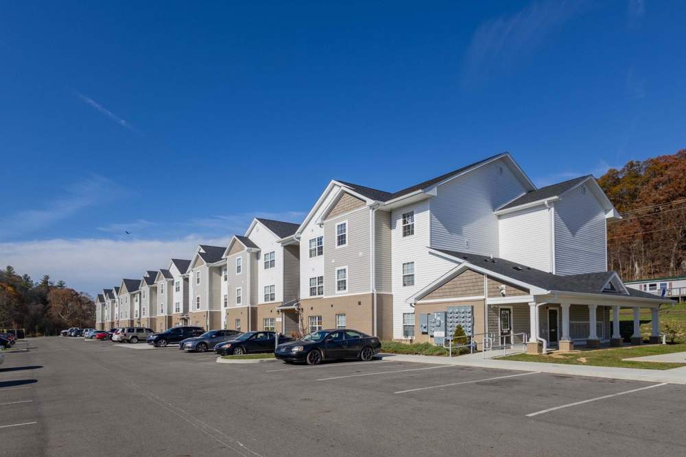 Apartment community with multiple buildings, parking spaces, and blue sky above at Kershaw Greene III in Athens, Ohio
