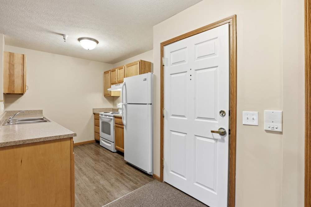 Bright kitchen featuring wood-style flooring, white appliances, and wooden cabinets with ample storage space at Norwood Greene Senior Living in Marietta, Ohio