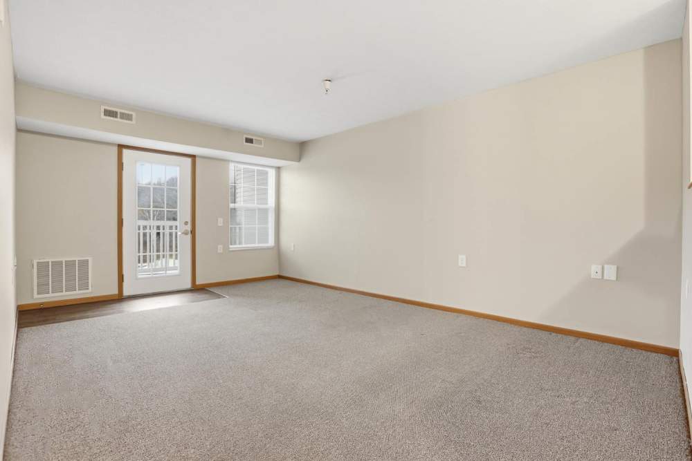 Spacious living room with carpeted flooring and balcony access through glass doors at Norwood Greene Senior Living in Marietta, Ohio