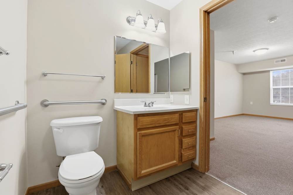Spacious bathroom featuring wood-style flooring, single vanity, and large mirror with natural light at Norwood Greene Senior Living in Marietta, Ohio