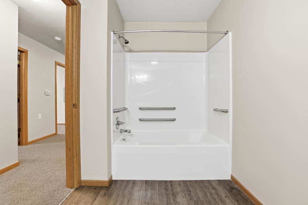 Bathroom with a white tub, safety grab bars, and wood-style flooring at Norwood Greene Senior Living in Marietta, Ohio