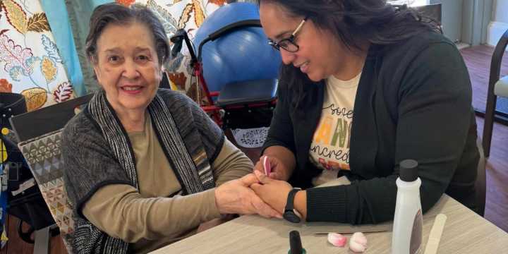 Resident receiving a manicure from a caring staff member at The Landing at Stone Oak in San Antonio, TX, during a pampering activity.