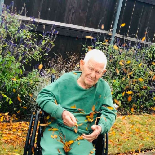 A Resident in a wheelchair sitting outside among falling leaves at Oxford Glen Memory Care at Sachse in Sachse, Texas