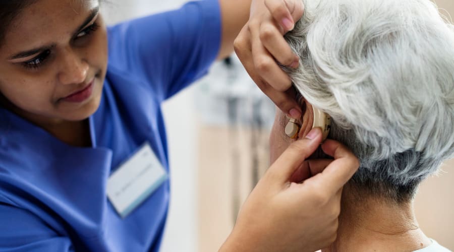 Certified nurse helping a resident with her hearing device at Peoples Senior Living in Tacoma, Washington