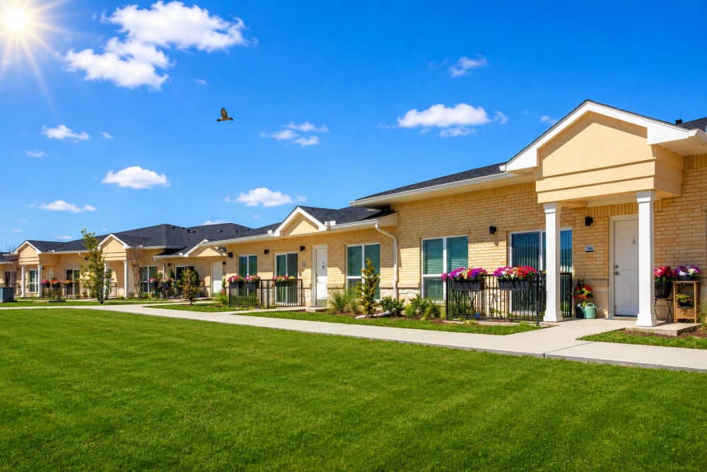 Single-story apartment community with green lawn, patio seating, and welcoming entrances at Springwood at Aliana in Richmond, Texas