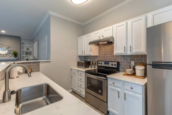 Fully equipped kitchen with white cabinetry, stainless-steel appliances, and tile backsplash at The Brandt in Irving, Texas