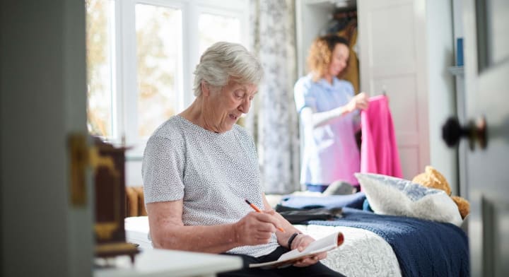 Senior writing while caregiver puts away clothes