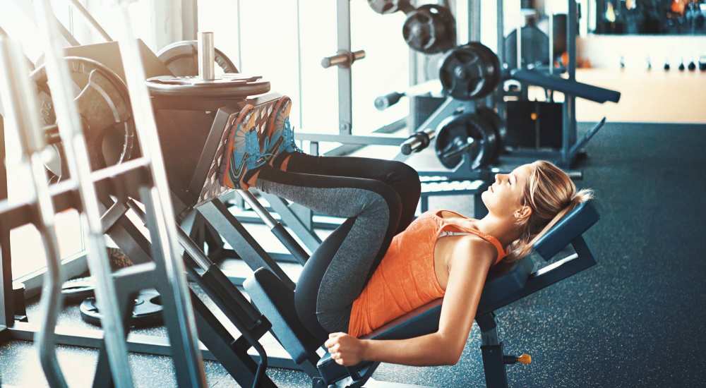 Resident doing leg press at the community fitness center at The Millwright in Cornelius, North Carolina