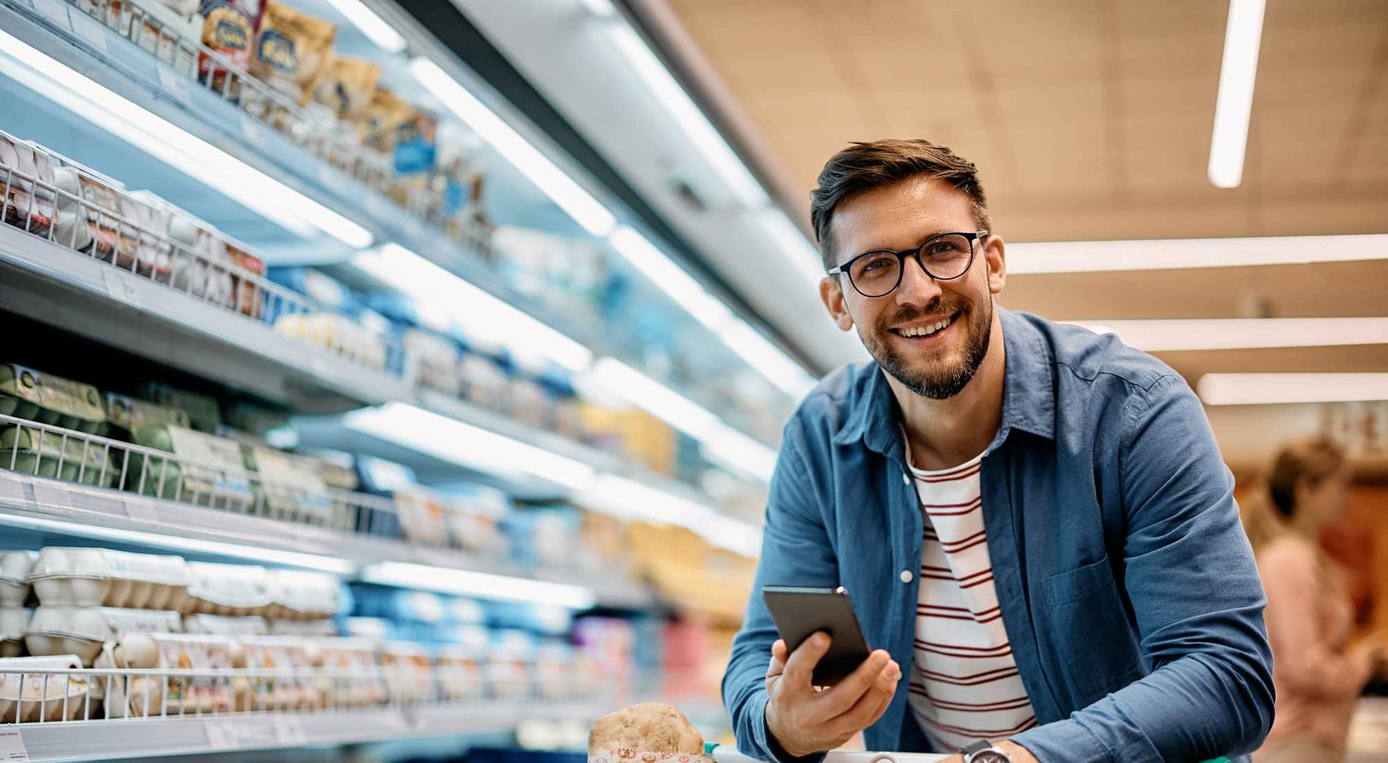 A man with glasses stands in a supermarket aisle, focused on his phone at Granite Creek in Rocklin, California.