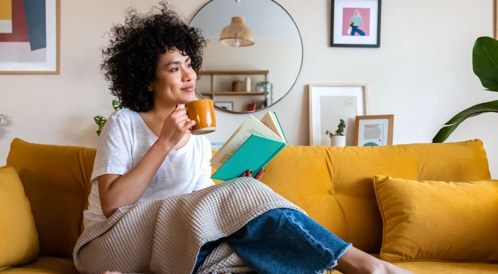 Resident enjoying coffee while reading a book in the living room at The Flats Of Donelson in Nashville, Tennessee