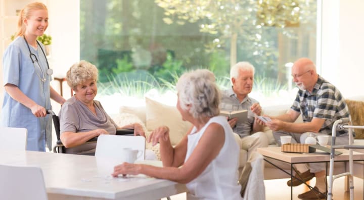 Senior woman in wheelchair smiling at friend while two senior men talk in the background