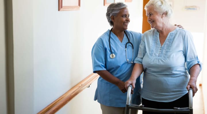 Caregiver and senior lady with walker smiling at each other