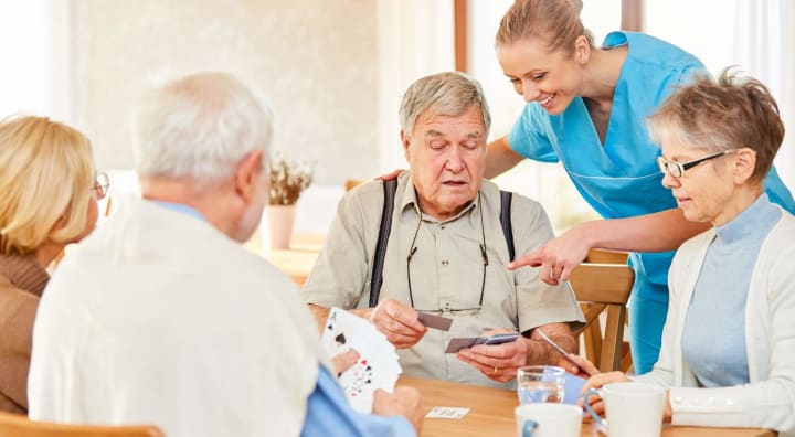 Two senior couples playing cards together with caregiver