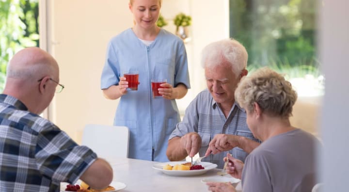 Three seniors eating while caregiver brings our drinks