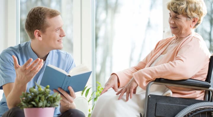 Caregiver reading to senior woman in wheelchair