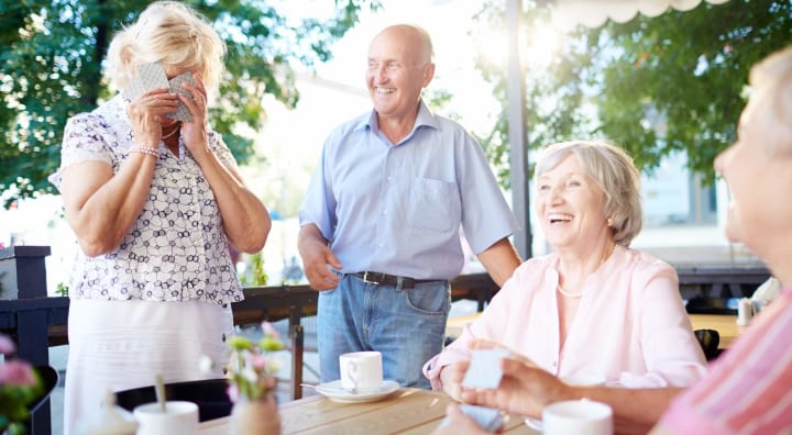 Senior woman covering her face with playing cards as other seniors laugh with her